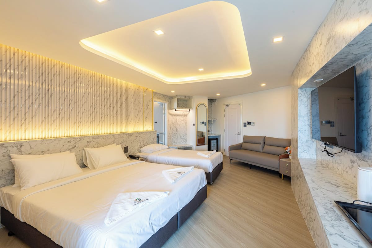Una habitación de hotel moderna con dos camas, un sofá, un televisor y un baño con pared de mármol.
