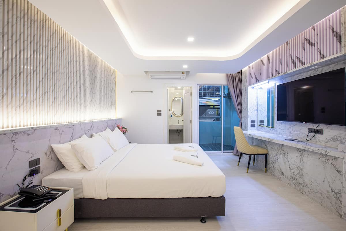 Habitación de hotel moderna con una cama grande, un televisor montado en la pared y un baño visible a través de una puerta abierta.