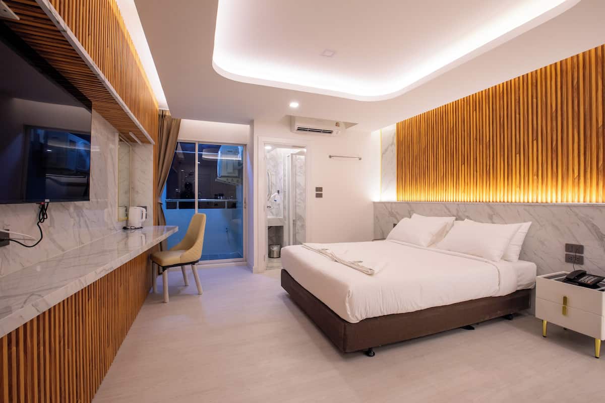Una habitación de hotel moderna con baño de mármol, una pared decorativa de madera y una cama con ropa de cama blanca.