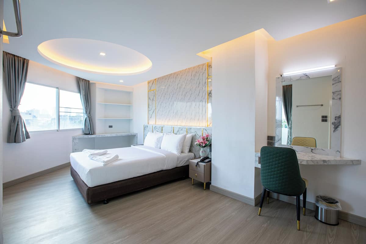Habitación de hotel moderna con una cama grande, mesitas de noche, un escritorio con silla, un espejo y vistas a la ciudad.
