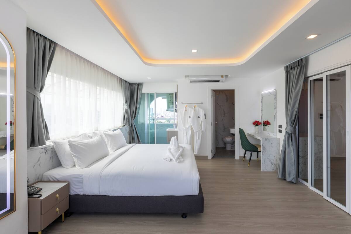Una habitación de hotel moderna con una cama grande, un tocador con espejo, un escritorio y un baño con inodoro y ducha.