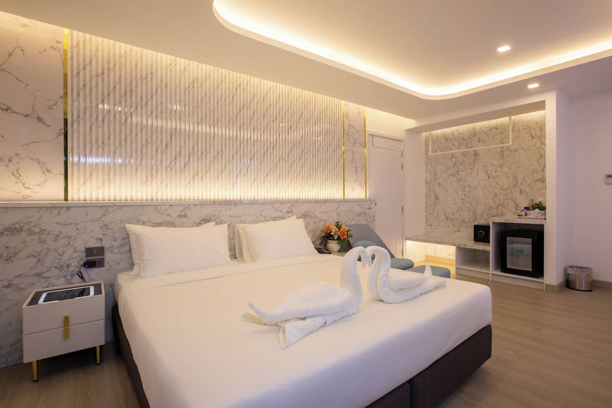 Una habitación de hotel moderna con una cama grande, una mesita de noche, televisión integrada y una pared de mármol.