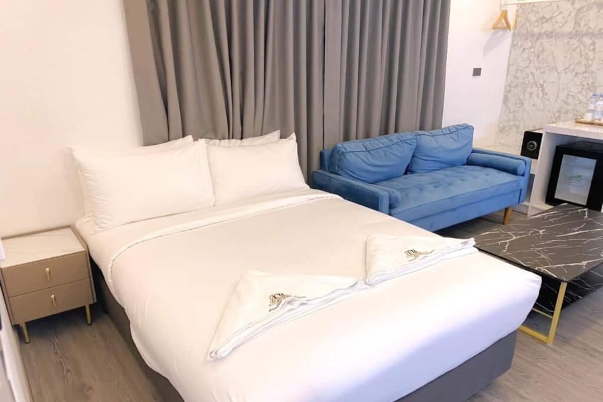 Una habitación de hotel con una cama, un sofá azul, un escritorio con una computadora y una pared de mármol.