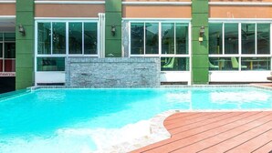 Una piscina con cubierta de madera, rodeada por un edificio con amplios ventanales y un muro de piedra.