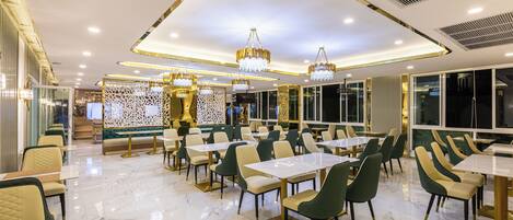 Un restaurante amplio con suelos de mármol, sillas verdes y beige, y detalles dorados.