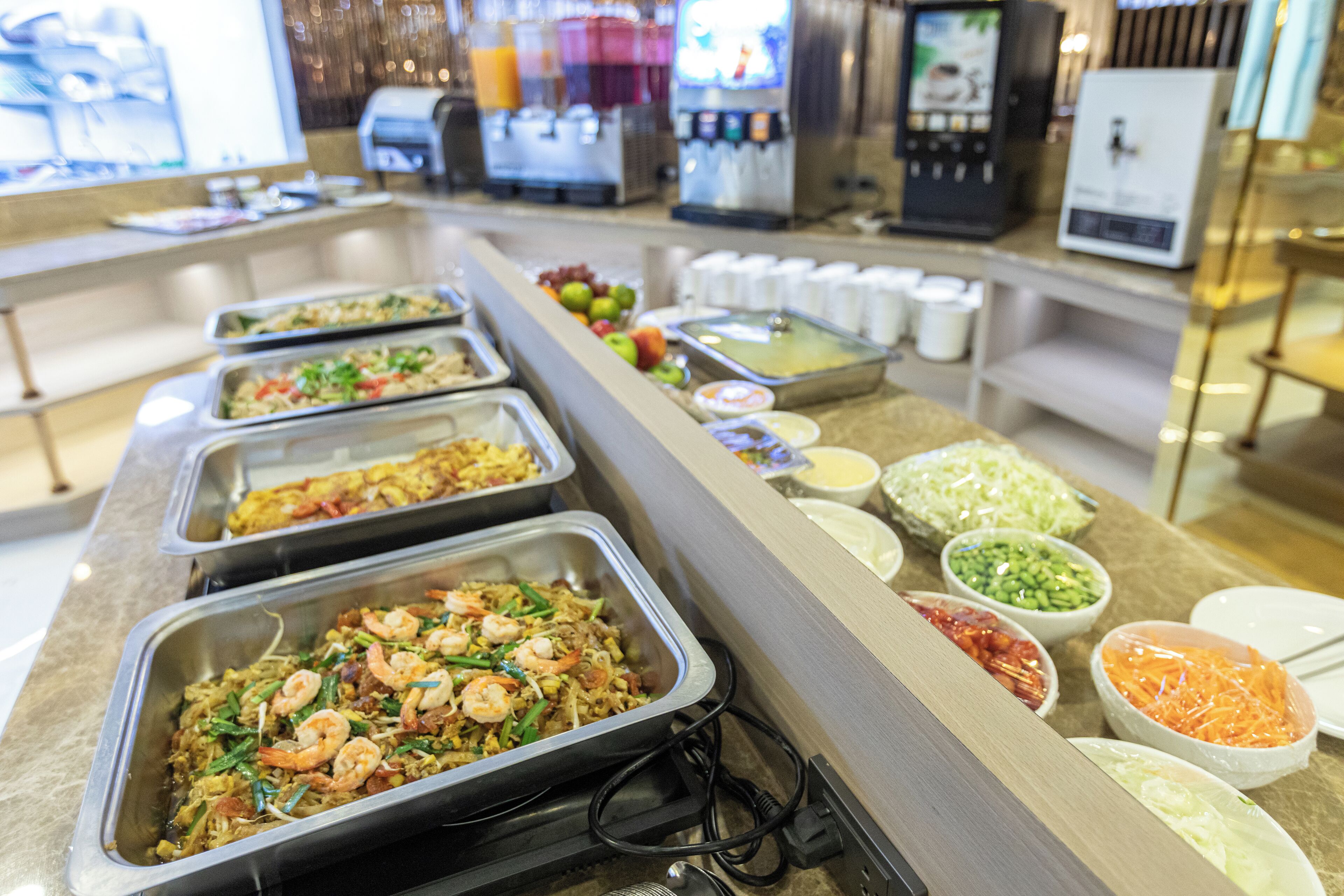 A buffet line with various dishes, including shrimp and vegetables, and condiments.