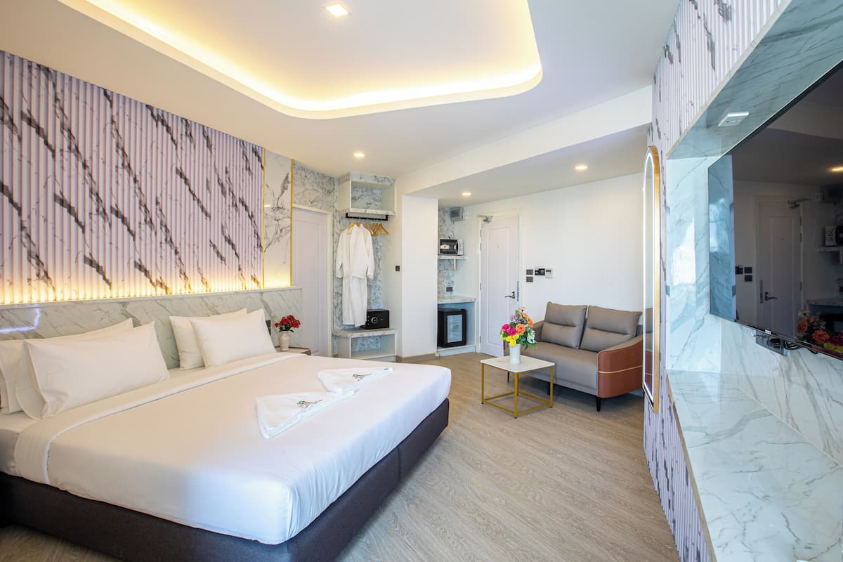 Una habitación de hotel moderna con una cama grande, una zona de estar con sofá, una pequeña mesa con un jarrón de flores y una encimera de mármol.