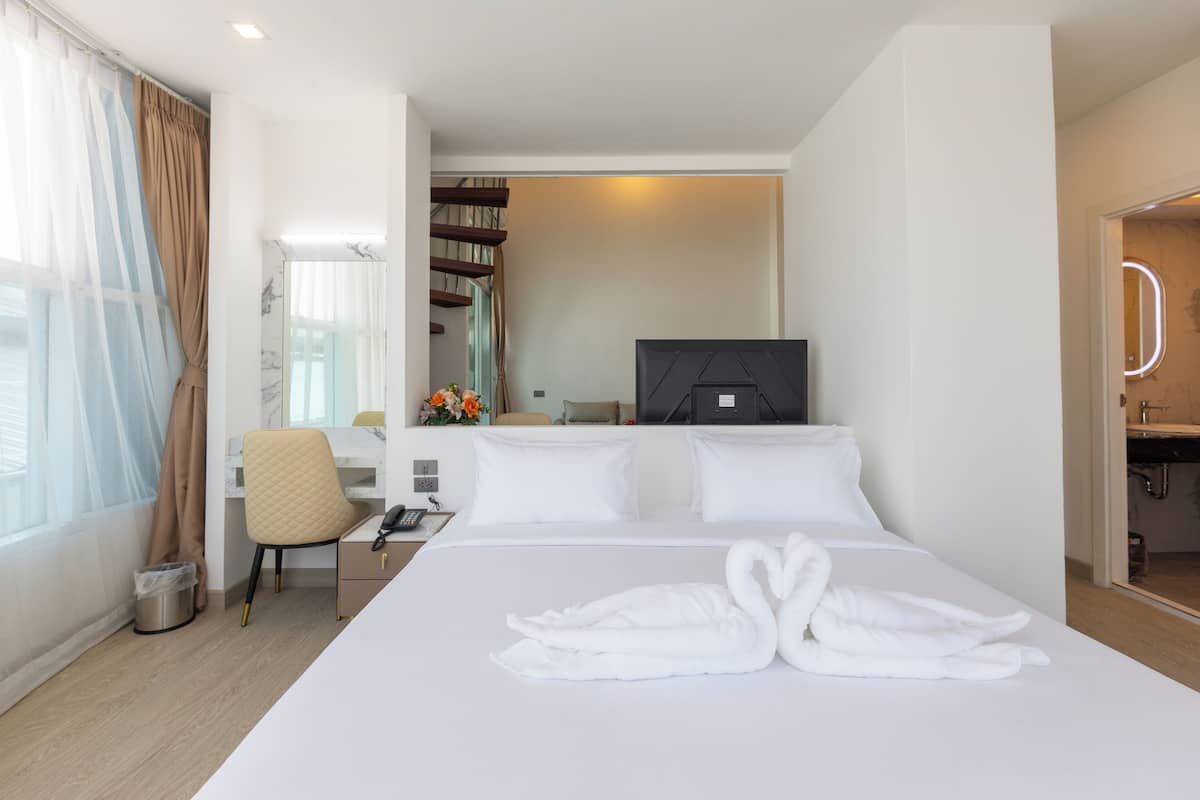 Habitación de hotel con una cama grande, un escritorio con una silla, un televisor y un baño visible a través de una puerta abierta.