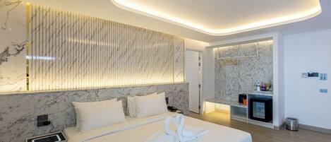 Una habitación de hotel moderna con una cama grande, pared de mármol y una pequeña zona de kitchenette.