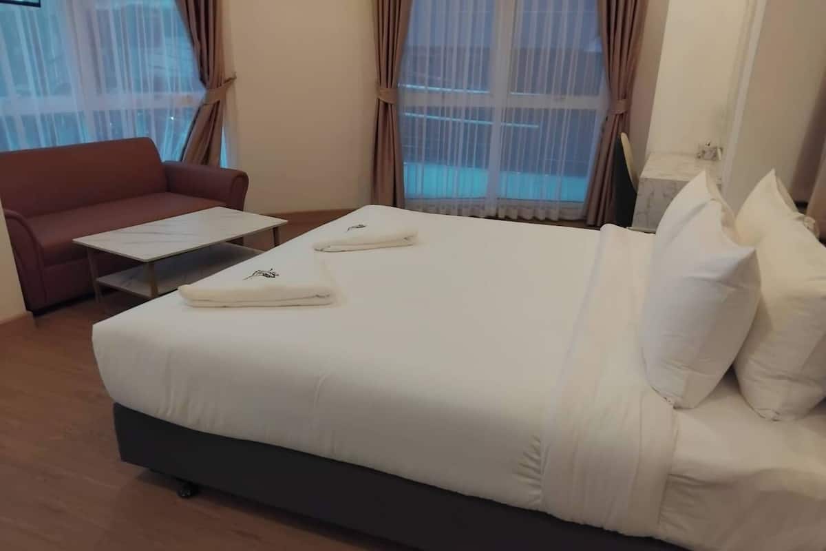 Una habitación de hotel con una cama grande, un sofá pequeño, una mesa de centro y cortinas en las ventanas.