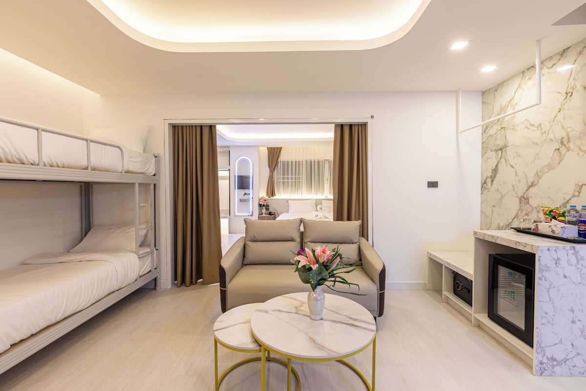 Una habitación de hotel moderna con una cama litera, un sofá, una pequeña mesa redonda con un jarrón y un minibar.
