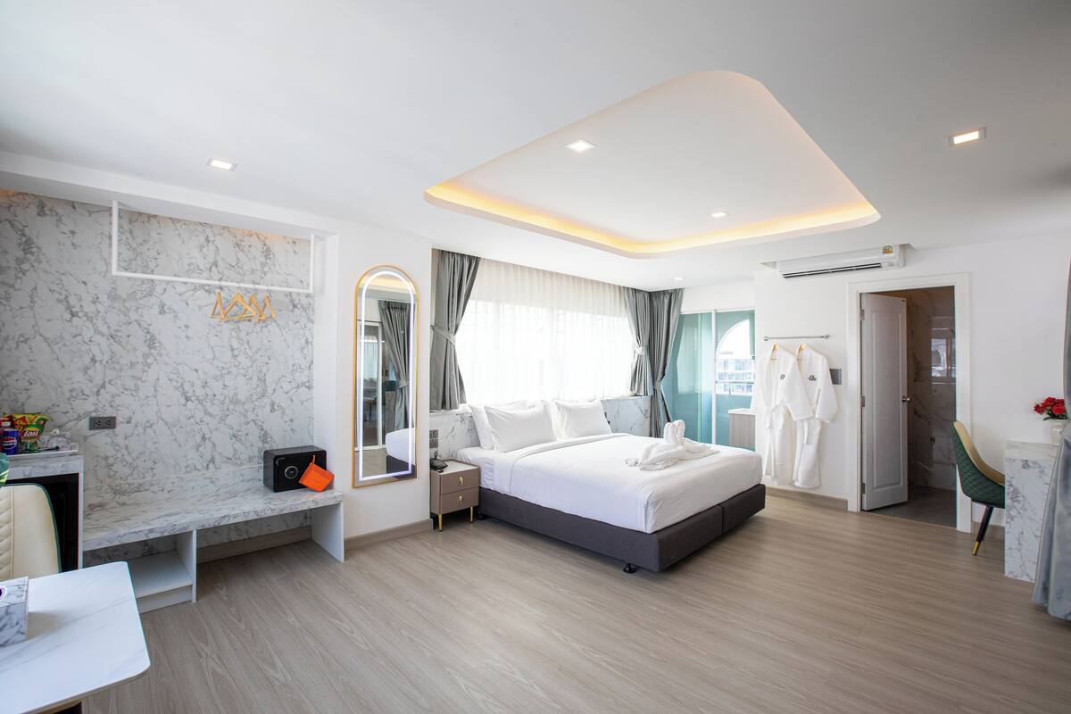 Una habitación de hotel moderna con una pared de mármol, una cama grande, una mesita de noche, un espejo y una zona de estar con un banco.