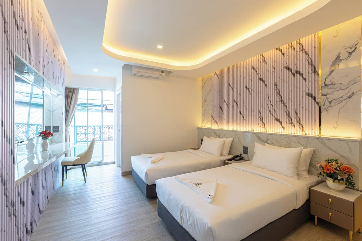 Habitación de hotel con dos camas, una zona de estar con una silla, un balcón con vistas y una pared de mármol.
