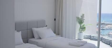 Ein modernes Hotelzimmer mit zwei Betten, einem großen Fenster mit Meerblick und einer Zimmerpflanze.