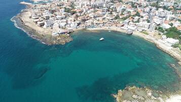 An aerial view of a coastal town with buildings along the shoreline, a clear blue sea, and a small boat in the water.