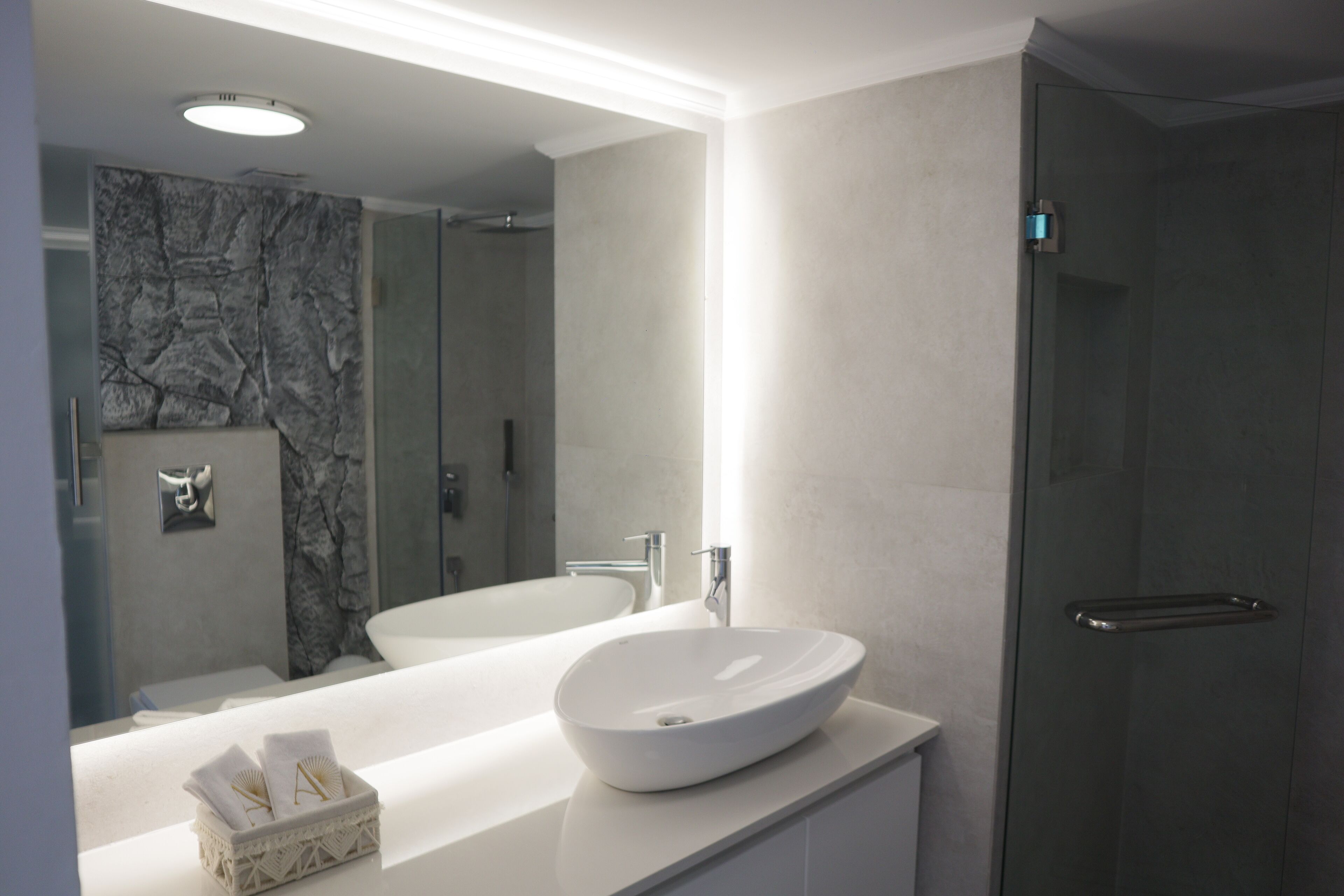 A modern bathroom with a large mirror, two sinks, and a walk-in shower.