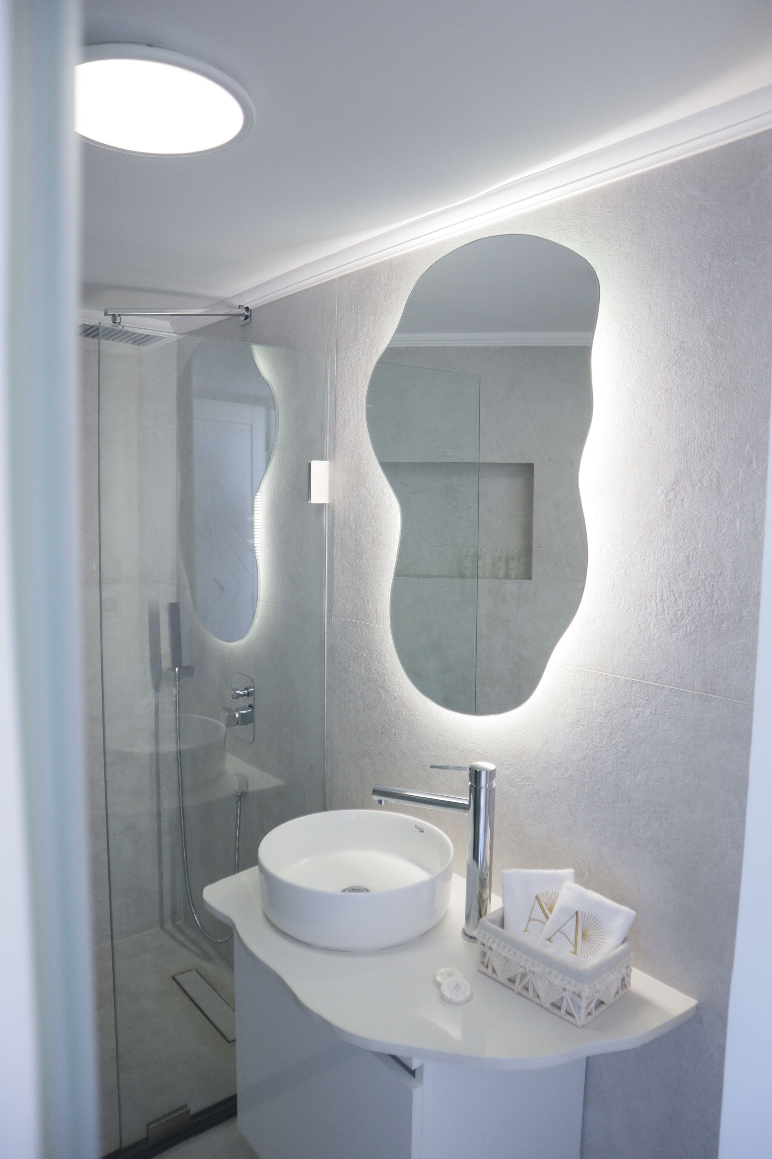 A modern bathroom with a glass-enclosed shower, a white sink, and a mirror with an integrated light.