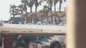 Una playa con palmeras, sombrillas y un litoral rocoso.