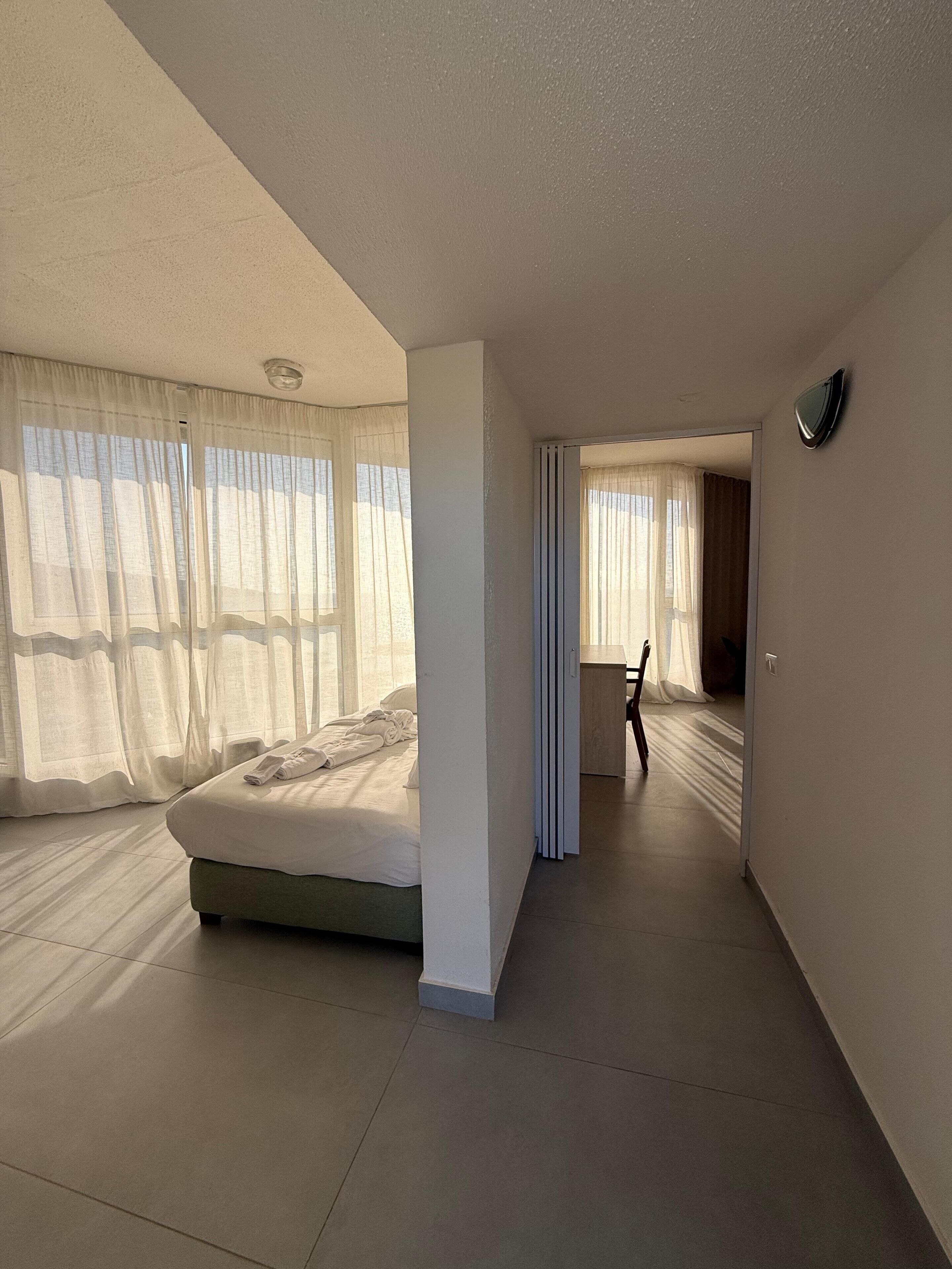 A modern hotel room with a large bed, a walk-in closet, and a view of the outdoors.