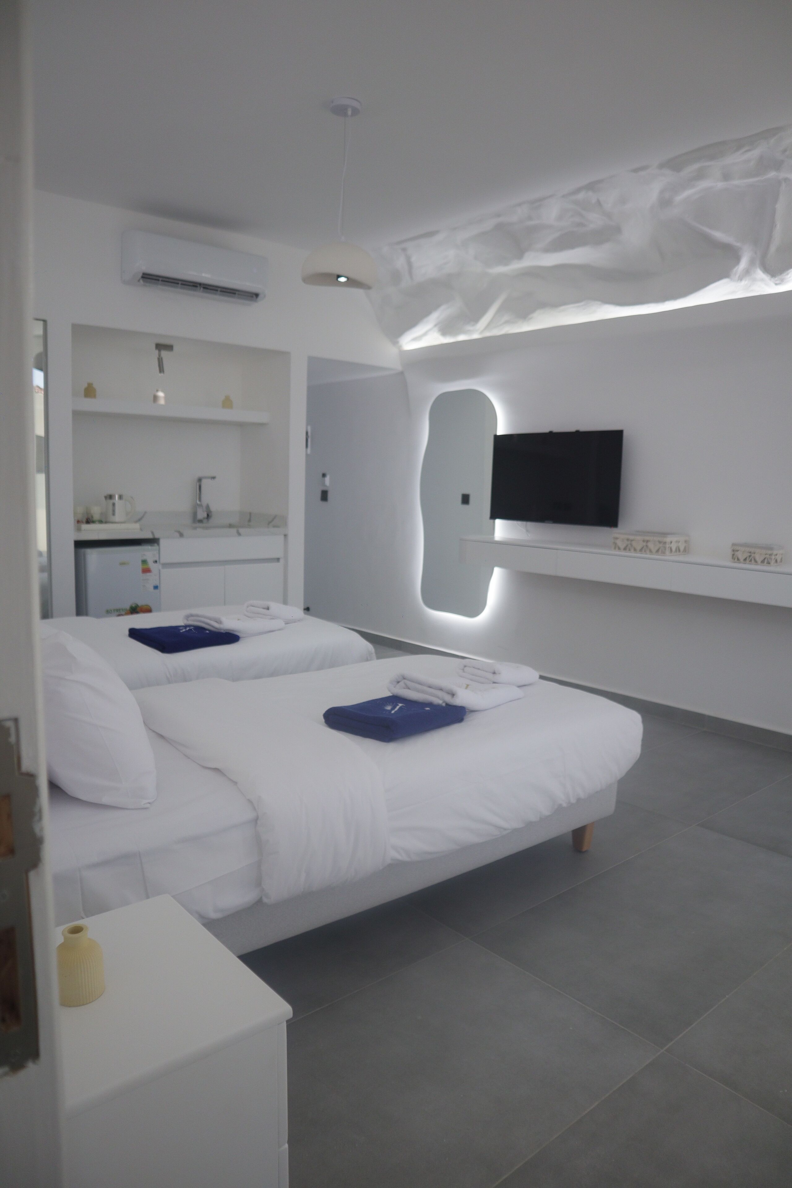 Een moderne hotelkamer met twee bedden, een aan de muur bevestigde televisie, een kleine kitchenette en een badkamer die door een open deur zichtbaar is.