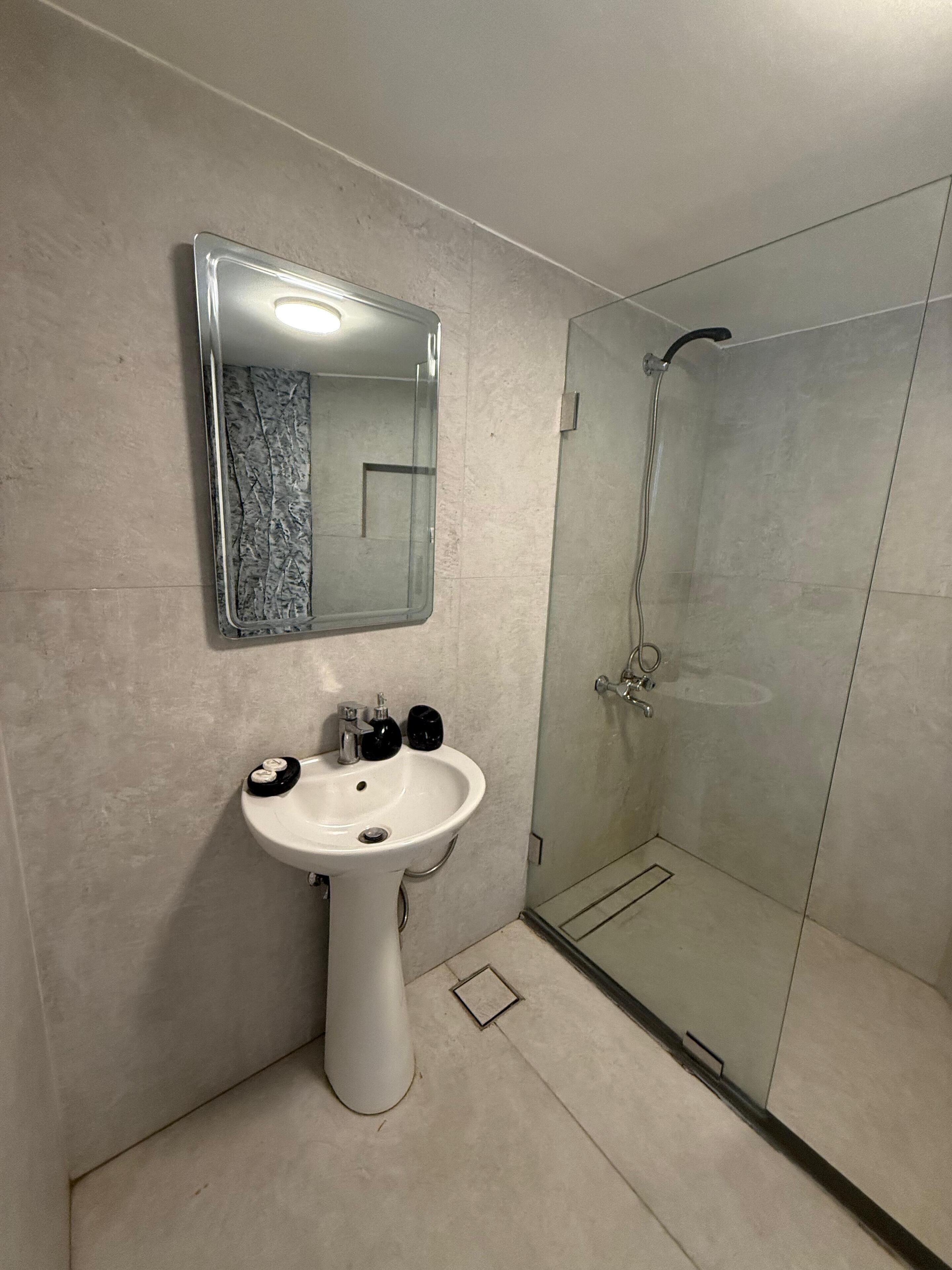 A modern bathroom with a pedestal sink, a mirror, and a glass-enclosed shower.