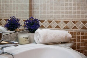 Un baño con un lavamanos blanco, una toalla blanca y una vela con forma de cactus.