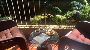 A balcony with two chairs, a glass table with a book, two cups, and a plate of cookies. - Casa ruya-Tierra (Benaulim)