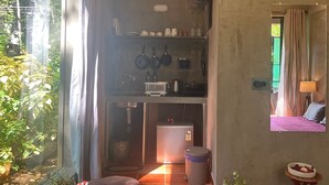 A compact kitchen with a sink, stove, and hanging pots. A small trash bin is visible, and a potted plant is on the floor. - Casa ruya-Tierra (Benaulim)