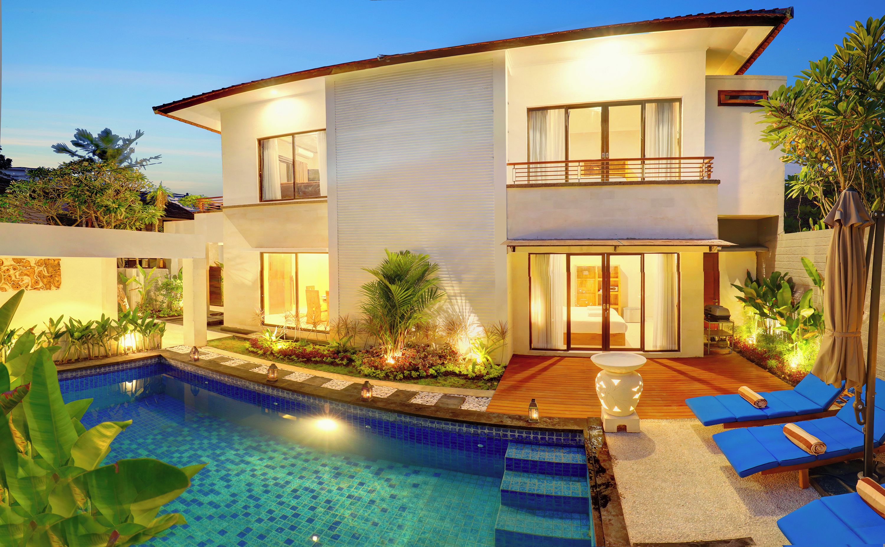 A modern two-story house with a swimming pool, outdoor seating, and a well-lit patio area.