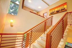 A staircase with wooden railings and white steps, a painting on the wall, and a window with a view of greenery. - Villa Alessandra Seminyak (Bali)