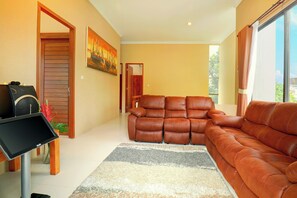 A living room with a brown leather sofa, a flat-screen TV, and a painting on the wall. - Villa Alessandra Seminyak (Bali)