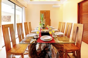 A dining table with chairs, a glass top, and a central floral arrangement. - Villa Alessandra Seminyak (Bali)