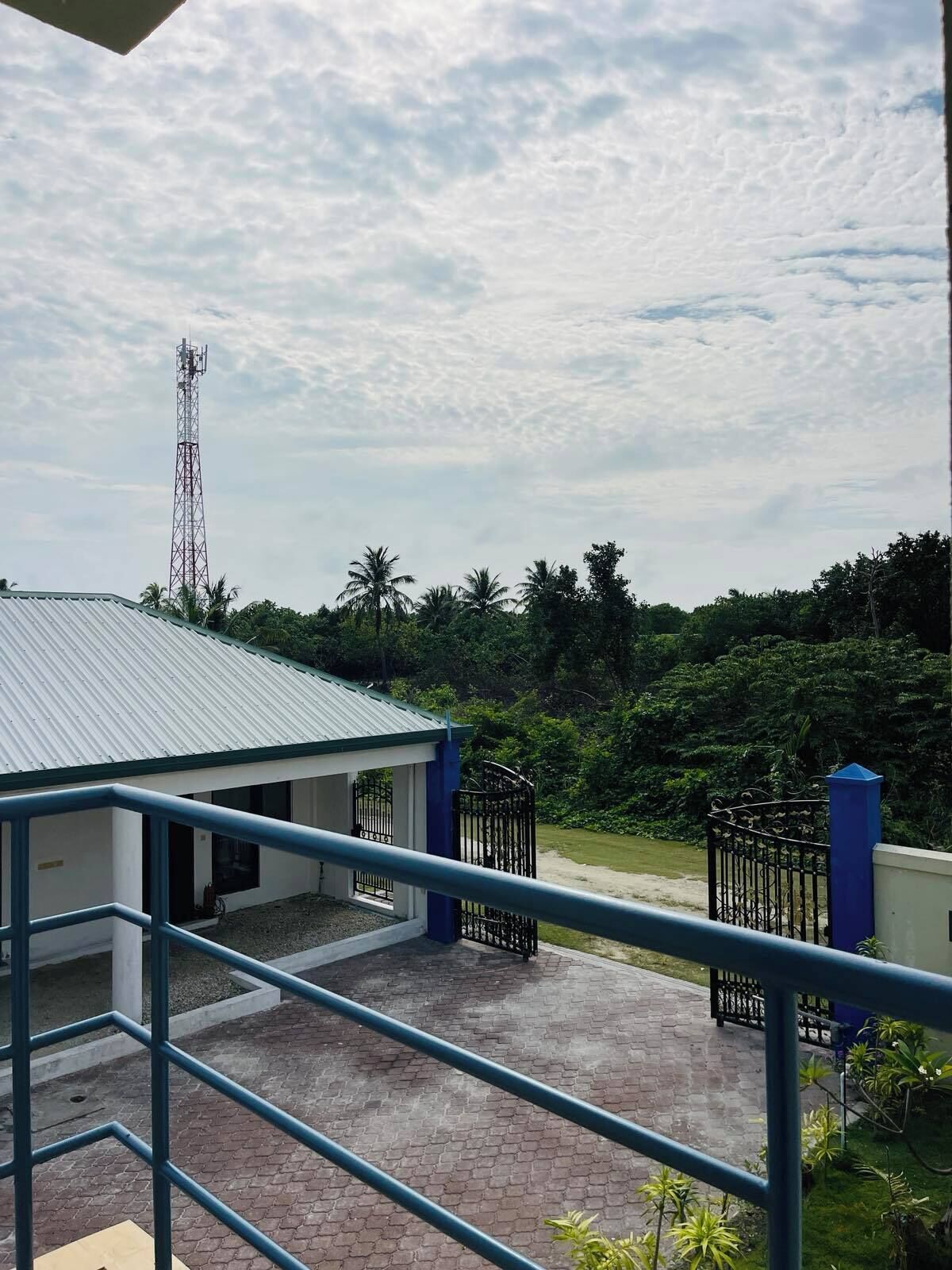 A building with a metal roof, a gated entrance, and a view of a tall communication tower in the background.