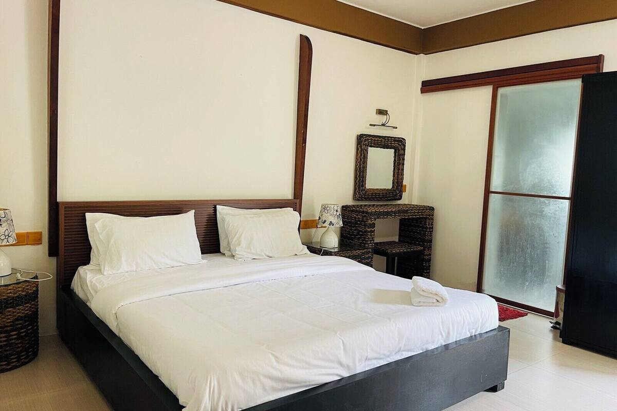 A large bed with white linens, a wooden headboard, a bedside table with a lamp, and a mirror on the wall.