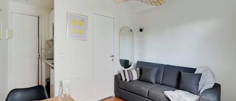 Ett modernt vardagsrum med en grå soffa, ett matbord i trä med stolar, en rosa vas och en takfläkt.