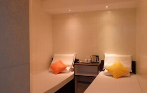 A small, clean room with two beds, each with a pillow, a nightstand with a lamp, and a small table with a cup and a book. - Hong Kong Full Harvest Inn (Kowloon)