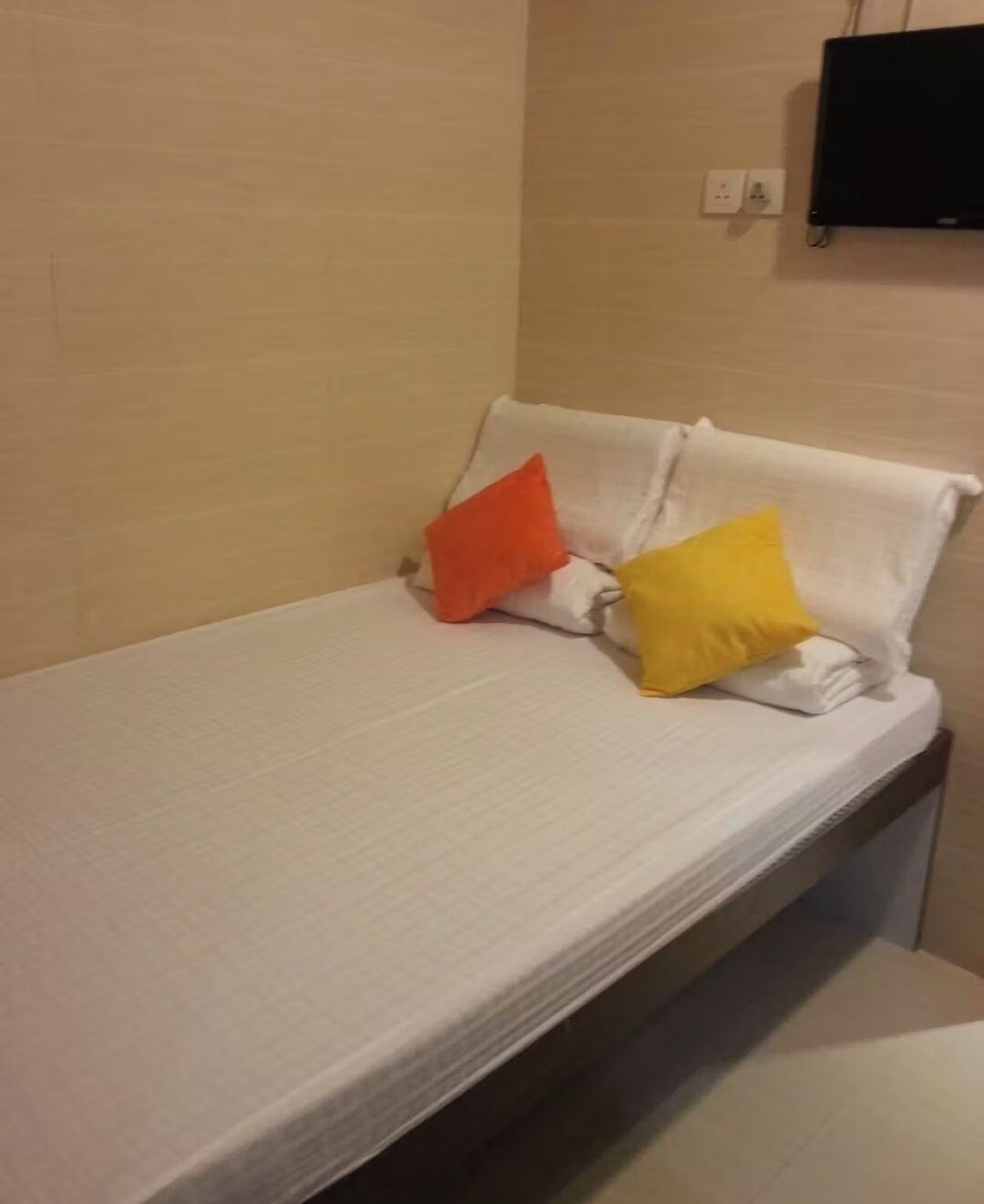 A single bed with white bedding and two pillows, one orange and one yellow.