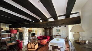 A rustic room with exposed wooden beams, a red sofa, a wooden table, and a bookshelf filled with books. - Le Mas d'Henriette  (Leyritz-Moncassin)