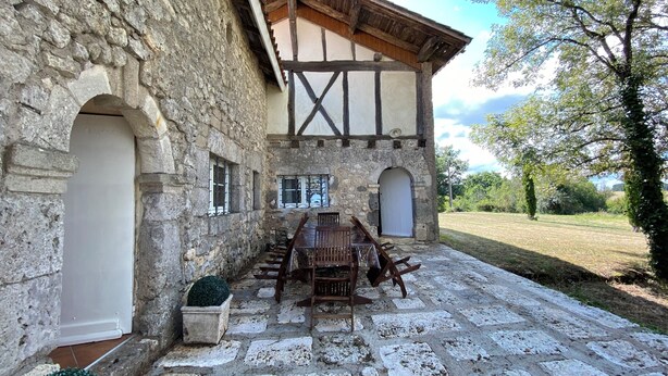 A stone building with a wooden balcony, a table with chairs, and a potted plant. - Le Mas d'Henriette  (Leyritz-Moncassin)