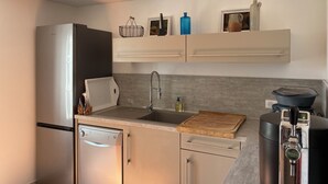 A modern kitchen with a built-in dishwasher, a stainless steel refrigerator, a sink with a wooden cutting board, and a coffee machine. - Le Mas d'Henriette  (Leyritz-Moncassin)