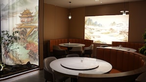 A restaurant with round tables and booths, featuring traditional Chinese artwork on the walls. - Renhe Hotel (Hangzhou)