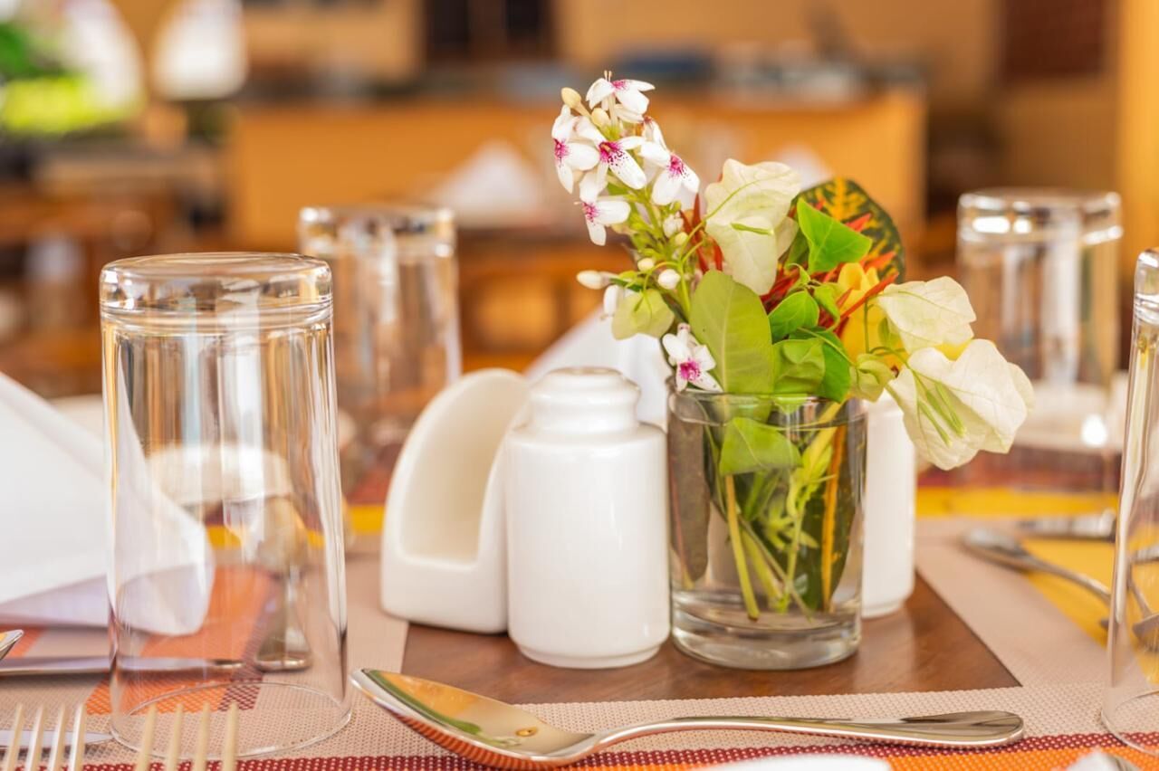 A dining table set with clear glassware, a vase with flowers, and salt and pepper shakers.