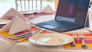 Una computadora portátil sobre una mesa, con vista a un paisaje tropical que incluye palmeras y un edificio con techo rojo.