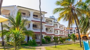 Un edificio de varios pisos con balcones, rodeado de palmeras y un cielo despejado.