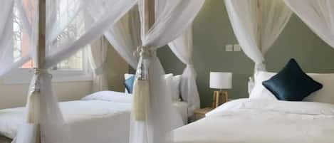 A room with two beds, each with a canopy bedspread. There is a small table with a lamp and a decorative rug on the floor.