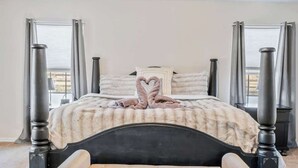 Una cama con dosel, con una toalla dispuesta en forma de corazón, un plaid blanco suave y vistas del exterior a través de una ventana con cortinas.