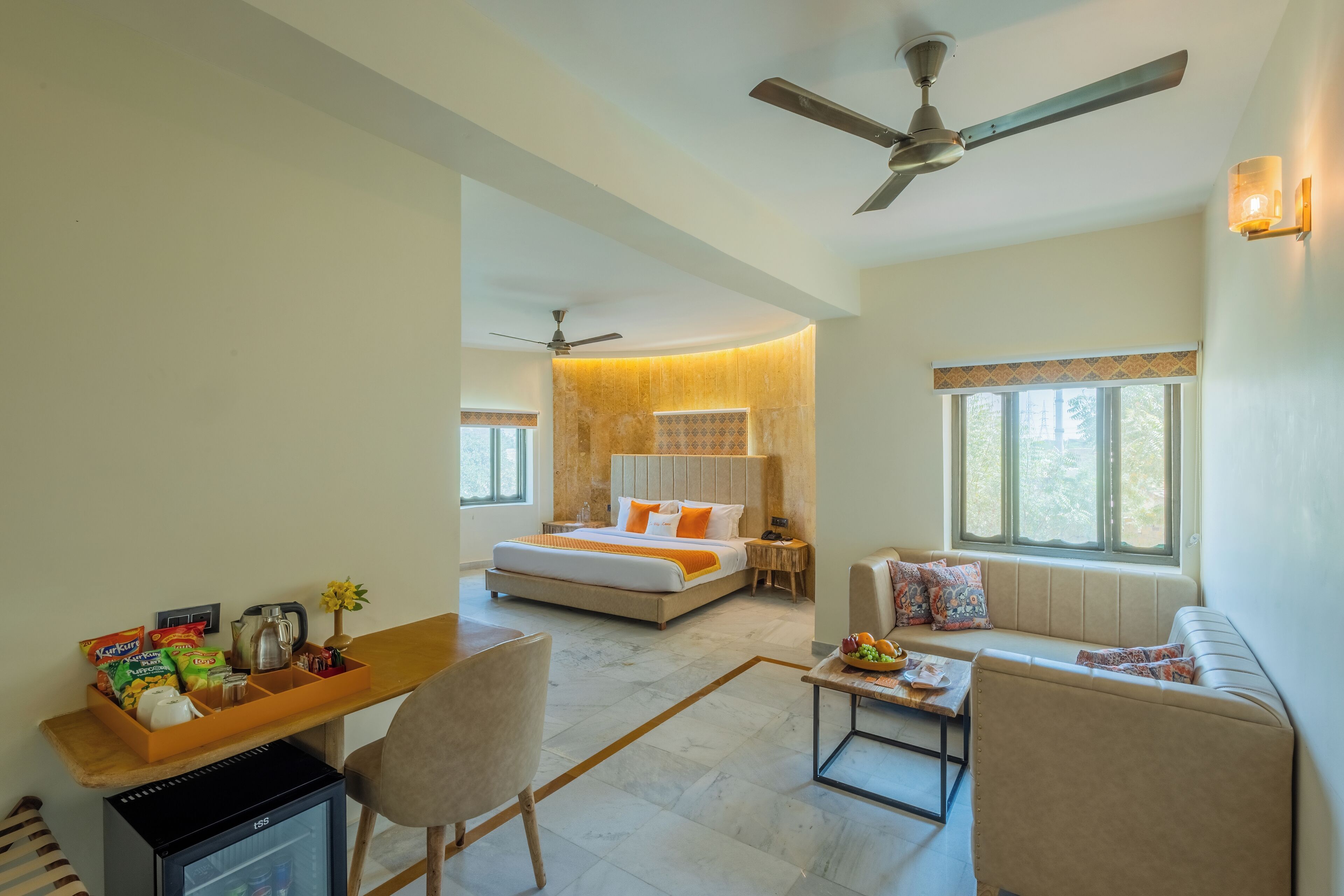 A hotel room with a bed, a desk with a computer, a sofa, a coffee table, and a ceiling fan.