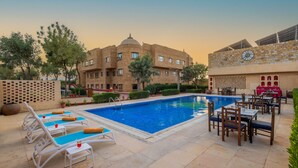 A swimming pool with lounge chairs and tables, surrounded by a building with a dome and solar panels. - Zone Connect by The Park Jaisalmer (Jaisalmer)