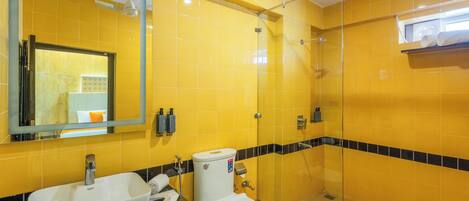 A bathroom with yellow tiles, a glass shower enclosure, a sink, and a toilet.
