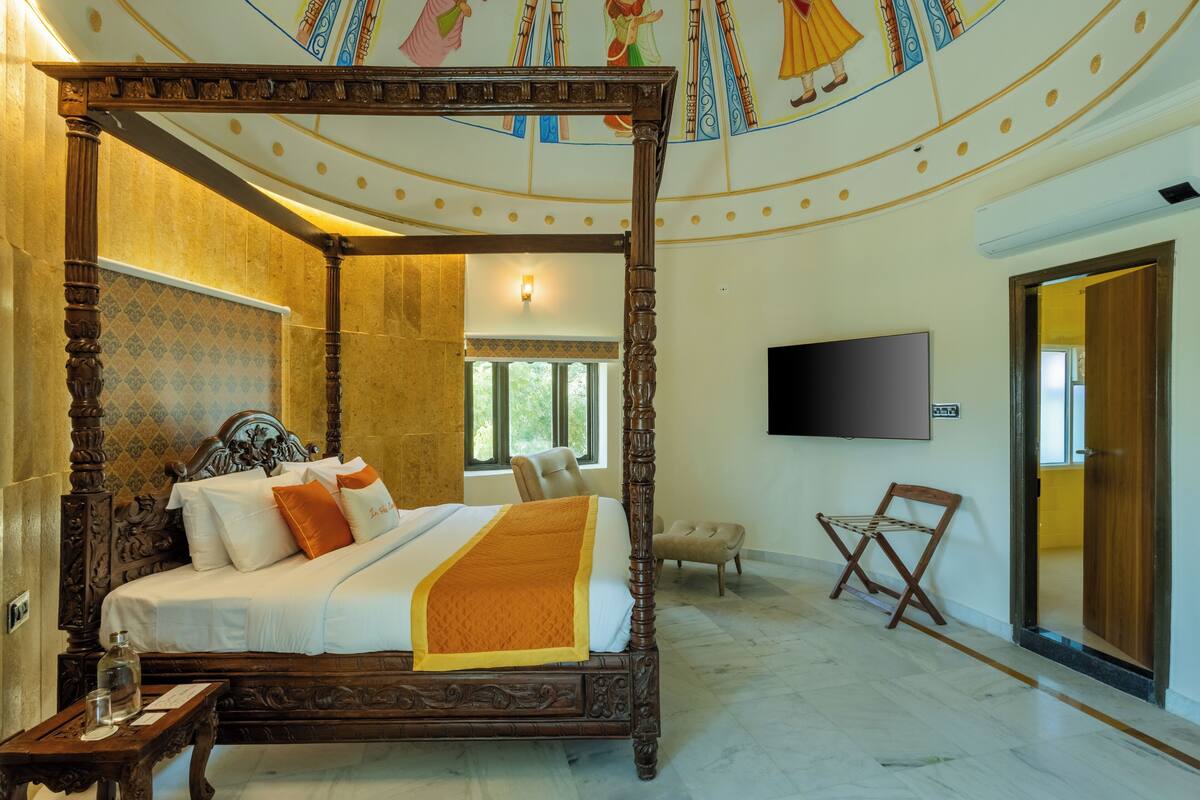 A four-poster bed with a wooden frame and white bedding, a flat-screen TV mounted on the wall, and a small wooden chair.